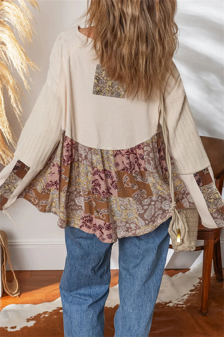 Back view of a woman wearing a beige paisley ethnic print top with patterned fabric and blue jeans.
